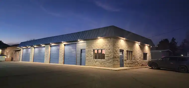 The Theisen shop at 1014 N 34th Ave in Yakima, stone-clad with blue roll-up bays, lit at dusk