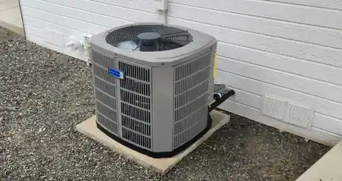 New American Standard condenser on gravel against white siding, close view