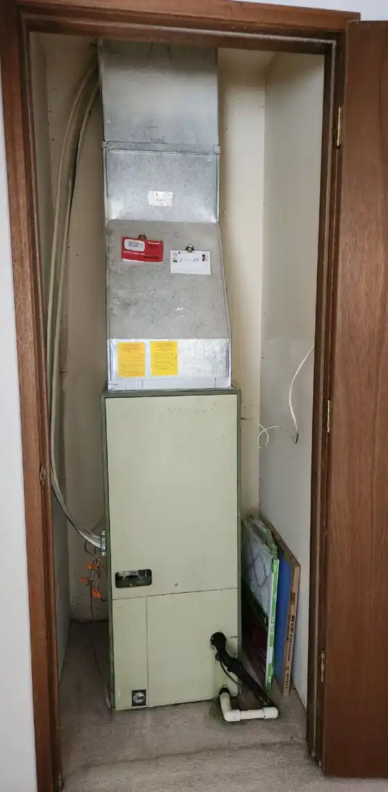 The old air handler standing in a wood-trimmed closet before the swap