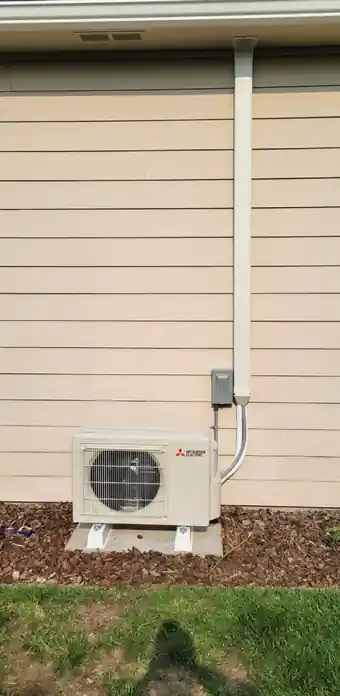 A Mitsubishi ductless outdoor unit mounted against beige lap siding.