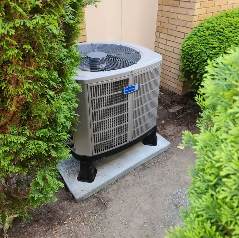 A new American Standard condenser set between shrubs against a yellow brick wall